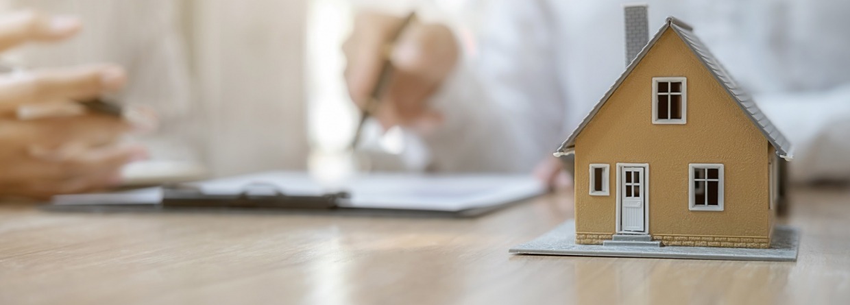 Een huis met op de achtergrond een adviseur in gesprek over de hypotheek