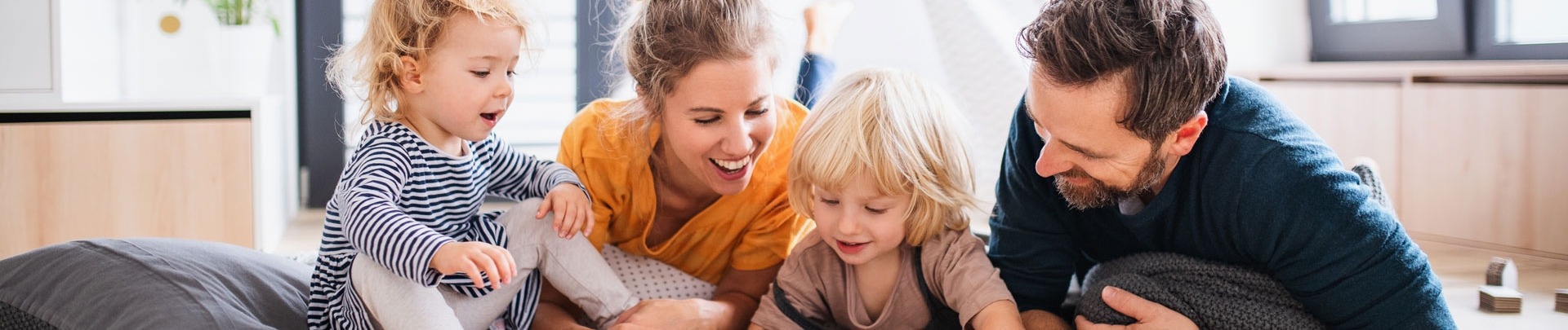 Jong gezin met twee kleine kinderen binnenshuis in de slaapkamer die een boek lezen.